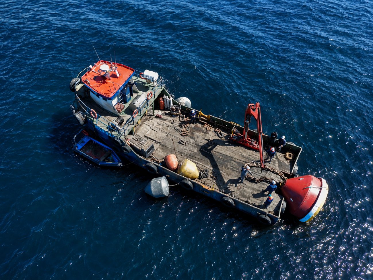 Vista aérea de embarcación de apoyo en faena de fondeo y traslado de boyas en mar abierto